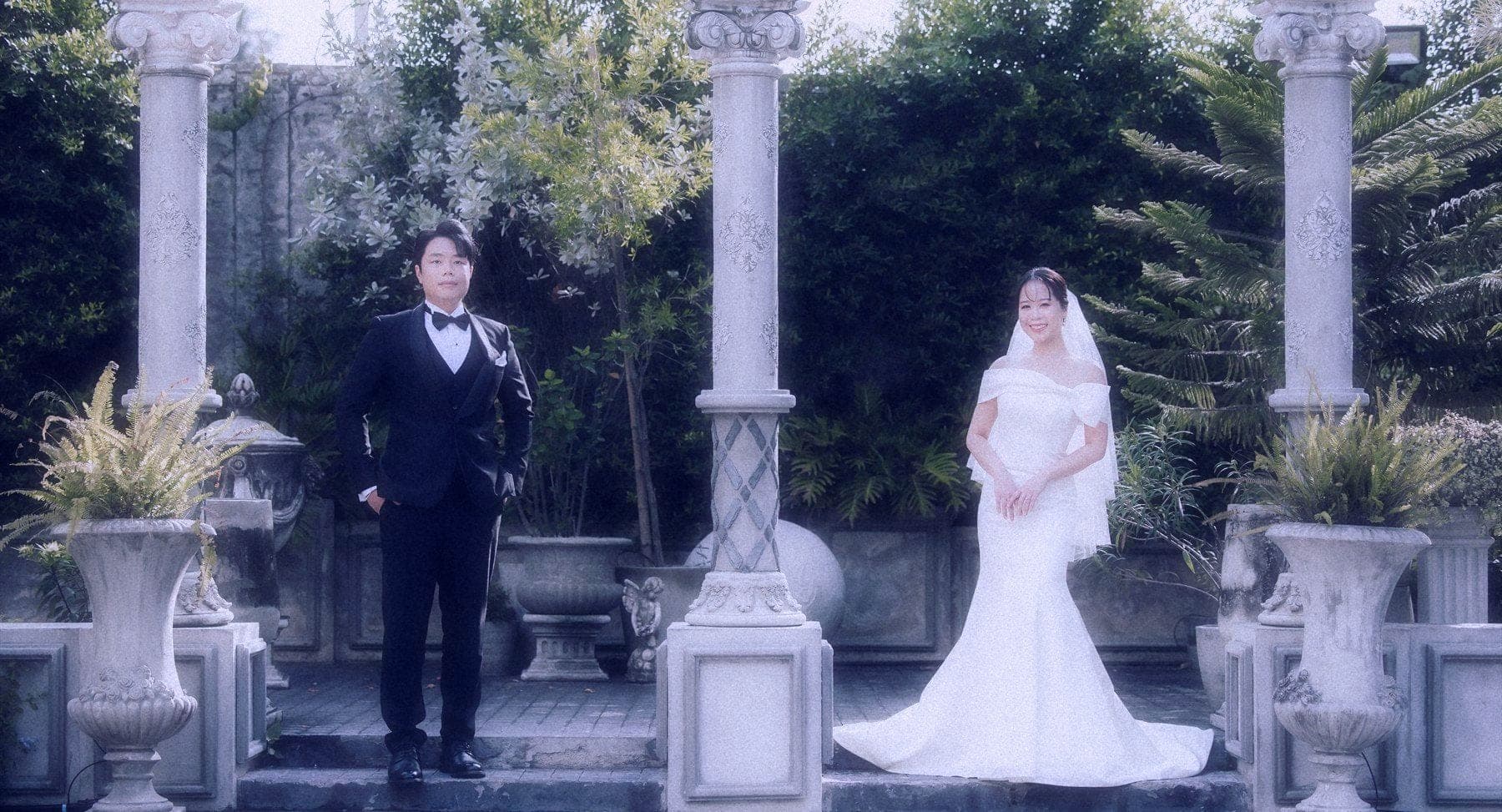 Witita and Sorratat standing between stone columns in a garden colonnade