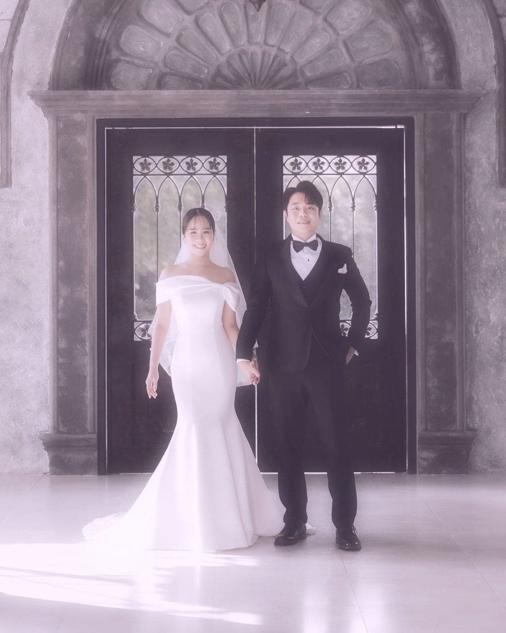 Witita and Sorratat in front of an arched iron door under a chandelier