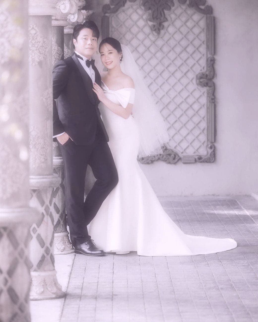 Witita in a mermaid gown and Sorratat beside stone columns and a lattice window