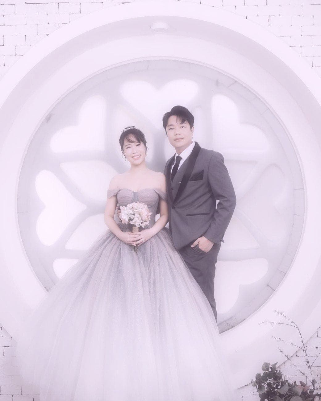 Witita in a grey tulle gown and Sorratat in front of a round rose window