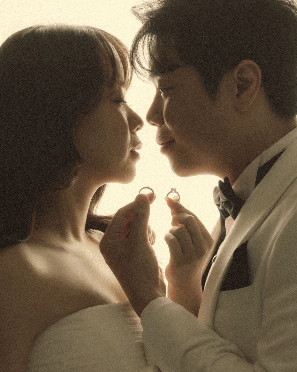 Witita and Sorratat nose to nose, each holding up a wedding ring