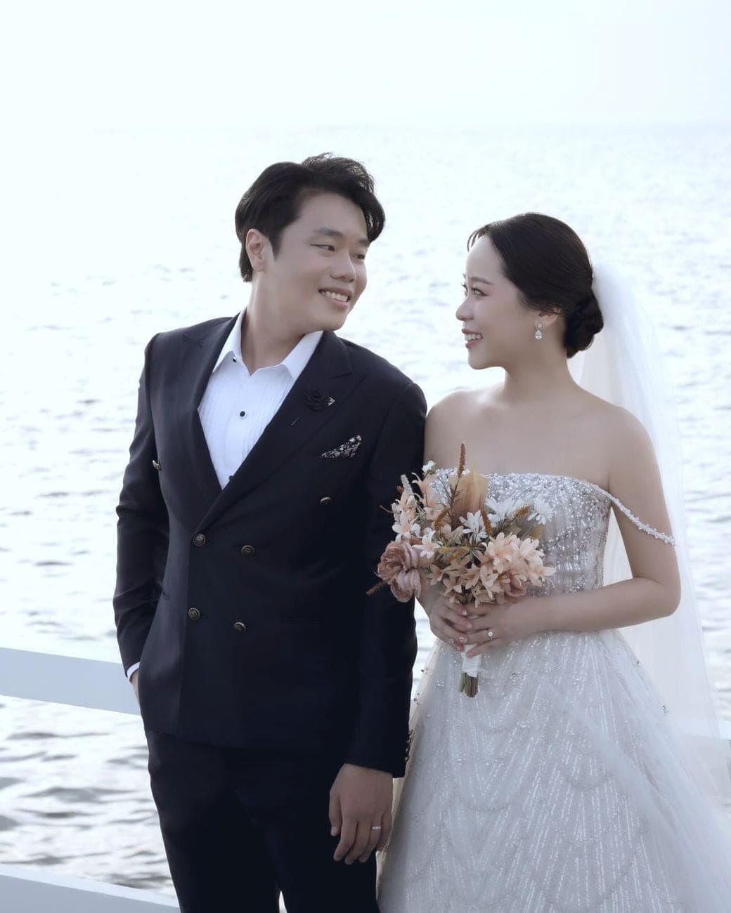 Witita with her bouquet and Sorratat by a white railing over the sea